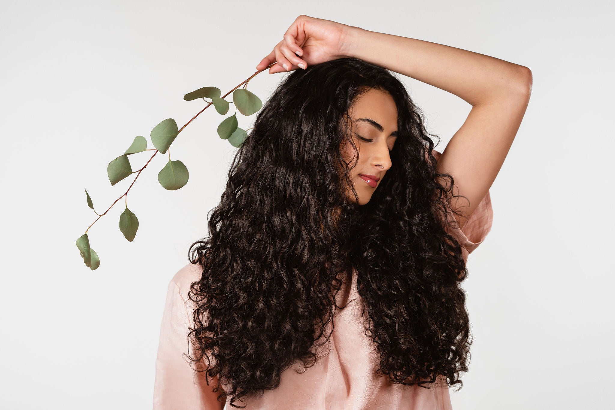 A woman with long curly hair and a piece of eucalyptus