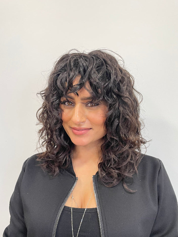 Curly hair shag haircut on dark hair, against a white wall.