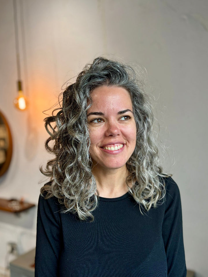 Woman with curly gray hair wearing a black top in an indoor setting.