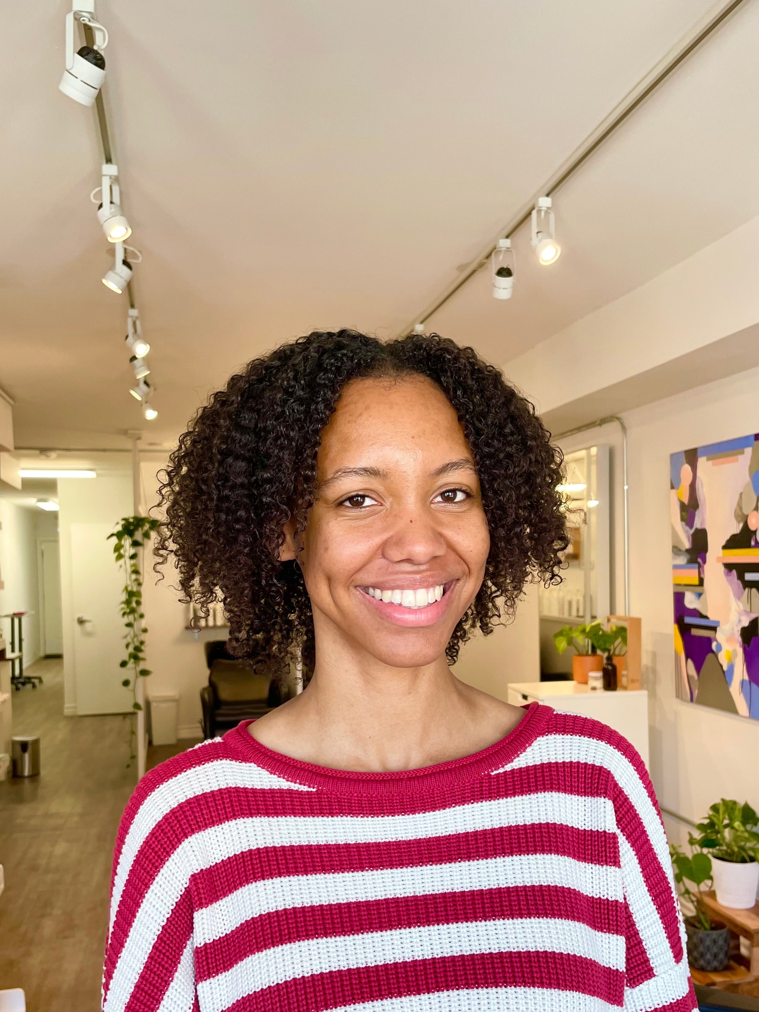 Woman wearing a red and white striped sweater in an indoor setting with plants and artwork.